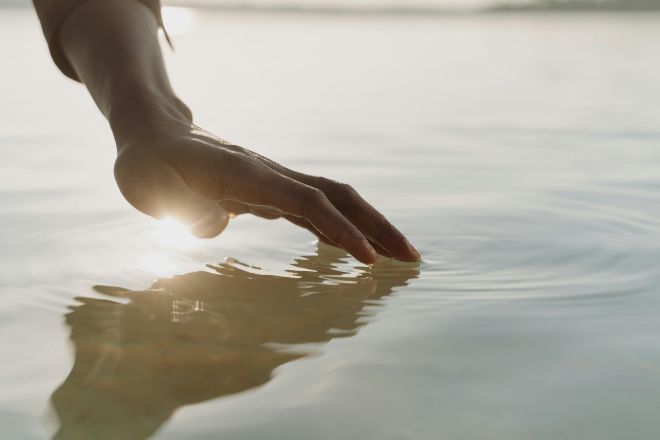 A tranquil scene of a hand gently touching the water, creating ripples with gentle sunlight reflection.