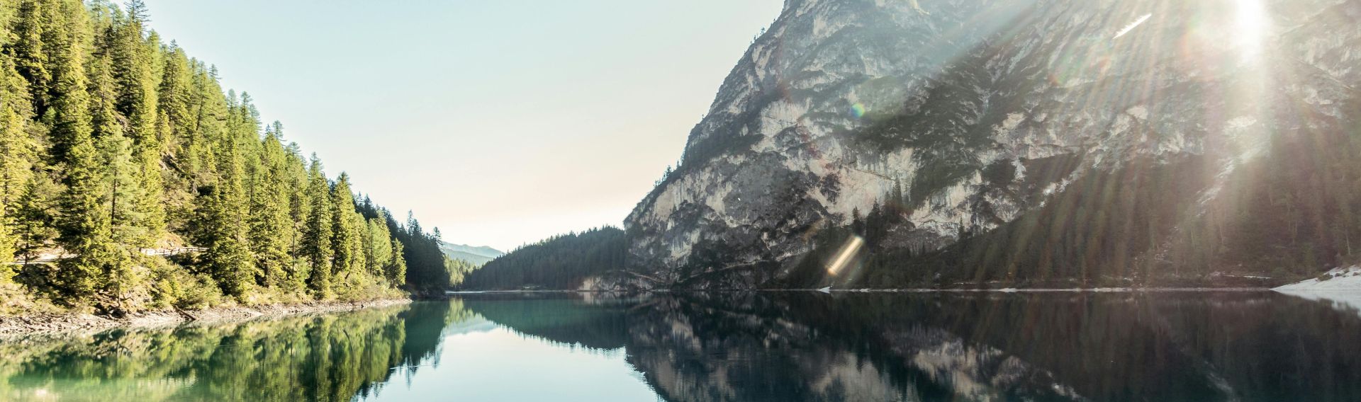 A serene mountain lake with clear reflections under the sunrise, creating a peaceful natural landscape.