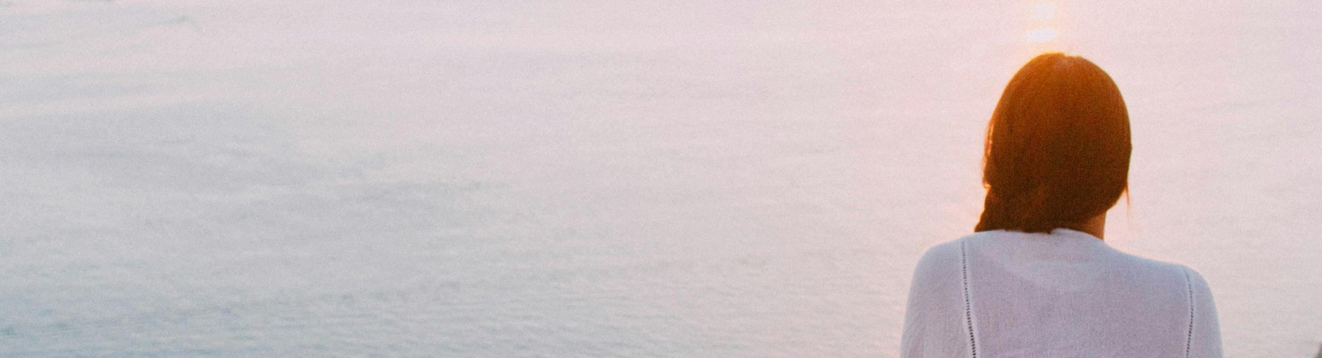 A serene view of a woman sitting on a rocky cliff, gazing at the ocean during sunset. Perfect for relaxation and travel themes.
